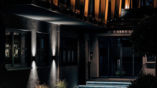 A modern building entrance with a dark facade, illuminated steps, and potted plants. - Hotel Alpenkönig (Oberstaufen)