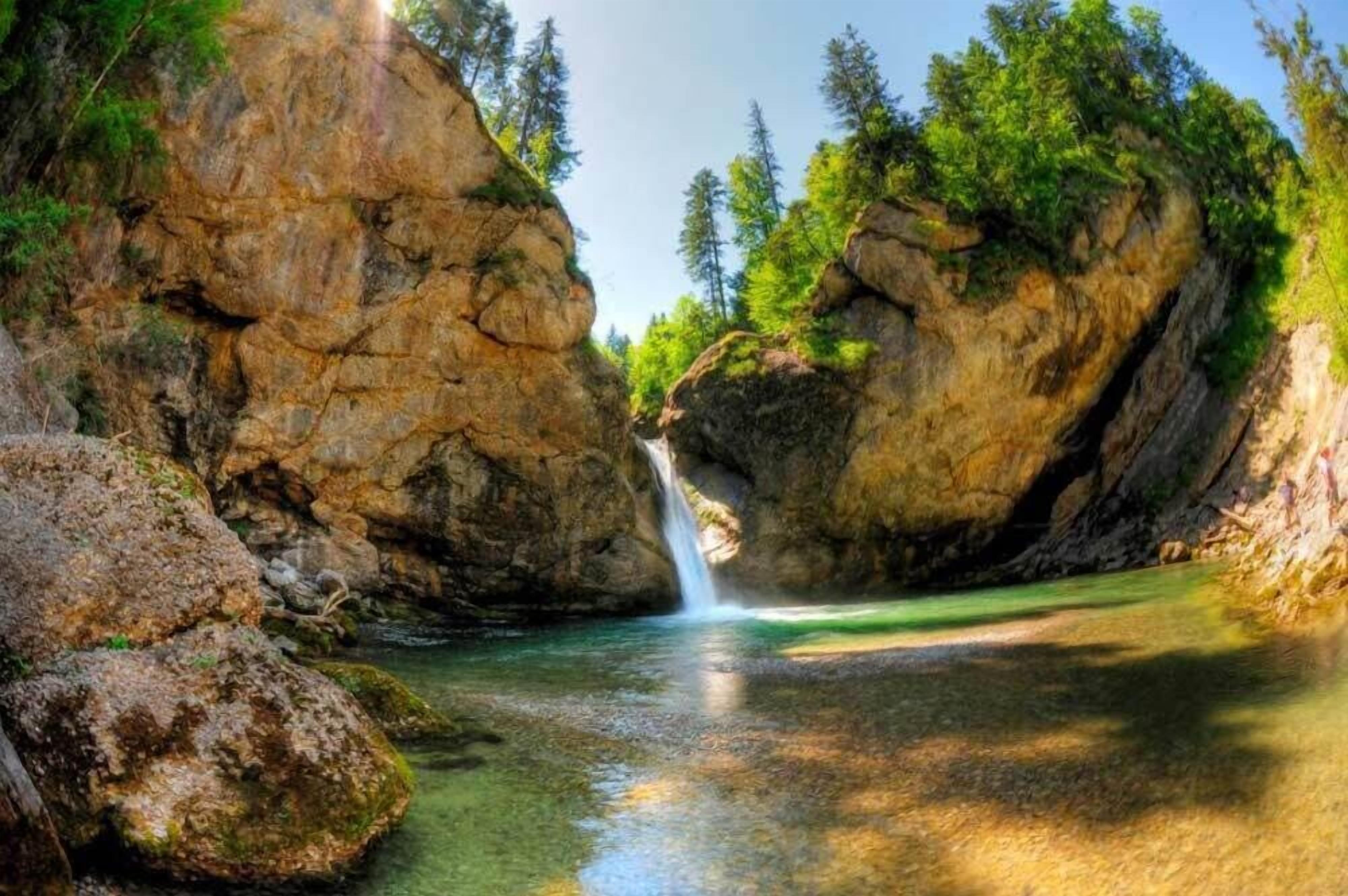 A natural landscape with a waterfall, rocky cliffs, and a clear pool of water.