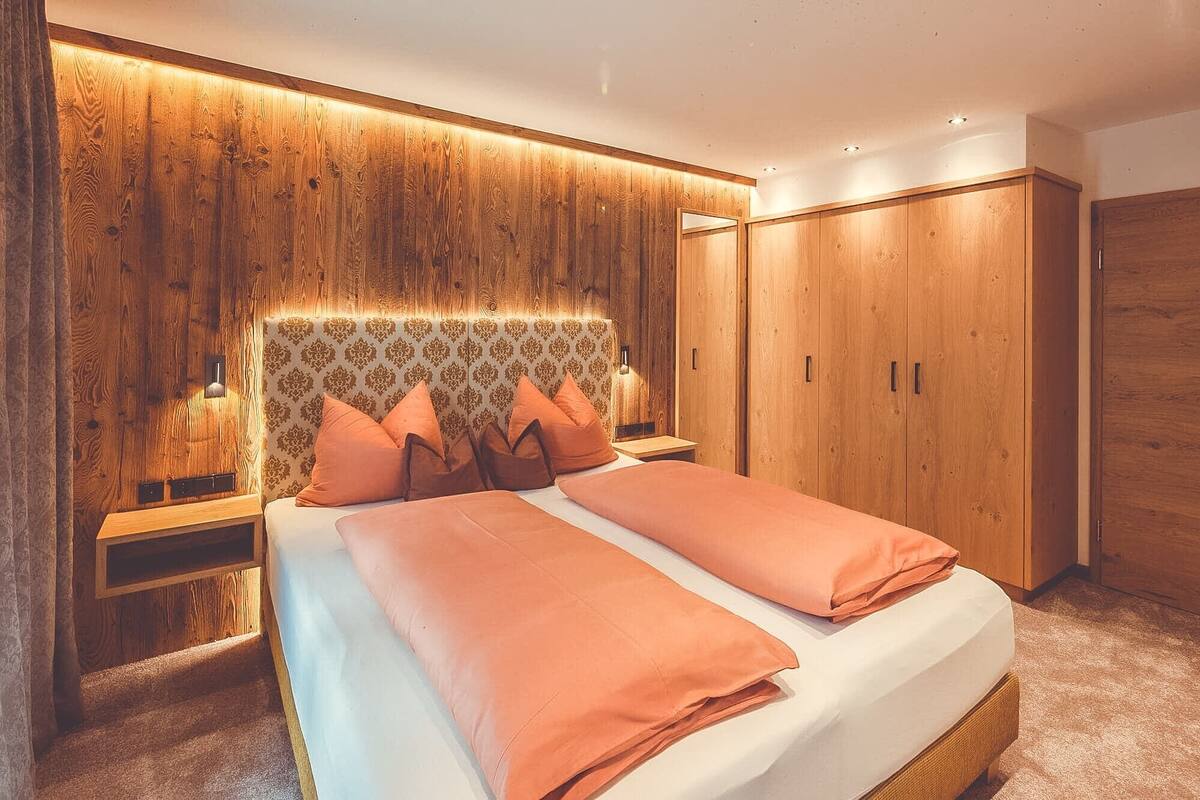 Une chambre à coucher avec une tête de lit en bois, un lit avec une literie orange et une armoire.