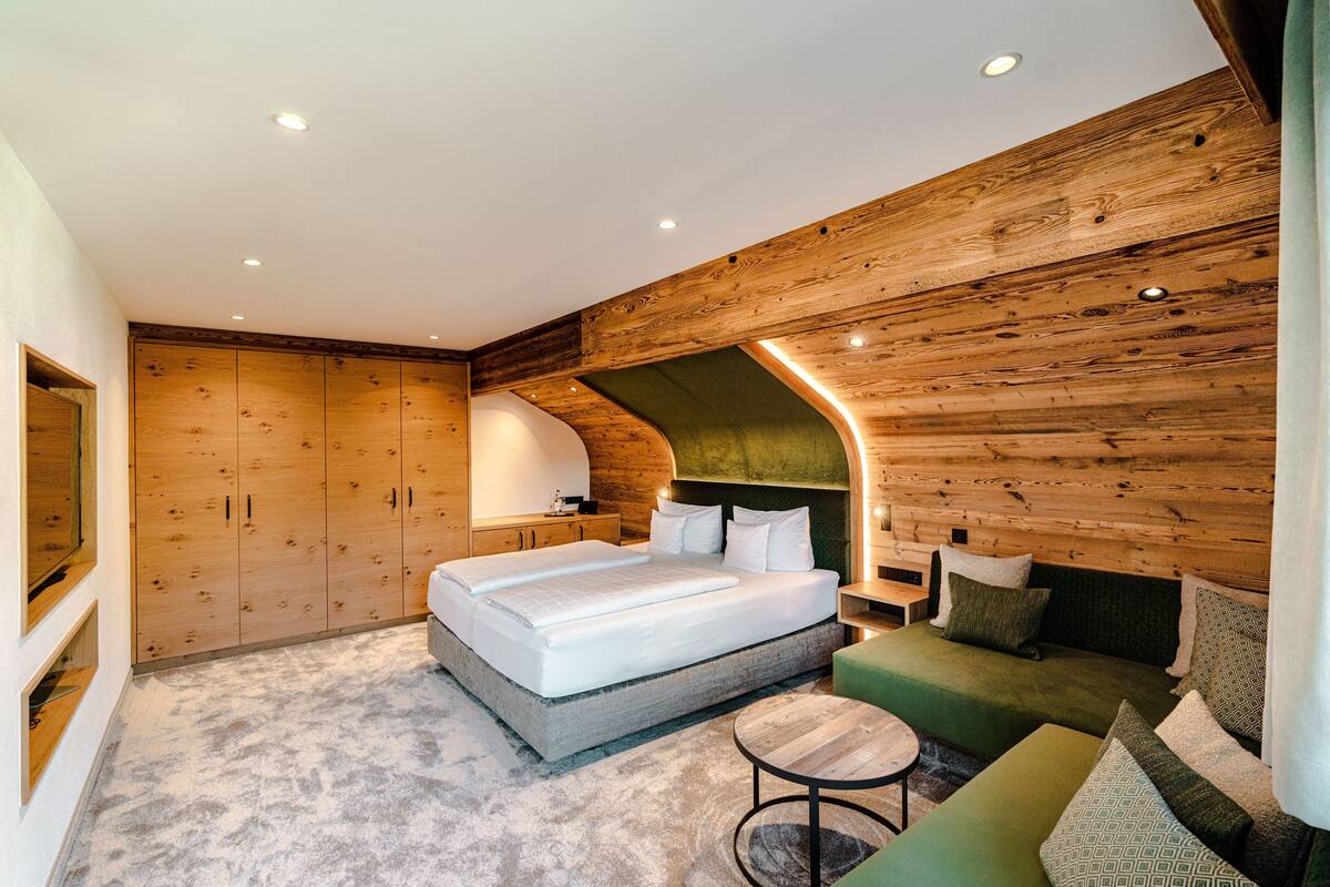 Une chambre à coucher moderne avec un plafond en bois, un grand lit, un canapé vert et une petite table ronde.