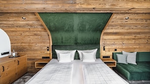 A double bed with a green upholstered headboard, a wooden nightstand, a green sofa, and a wooden dresser. - Hotel Alpenkönig (Oberstaufen)