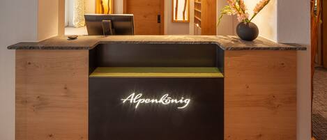 Un mostrador de recepción con detalles de madera, un letrero de neón que dice "Alpenkönig" y un florero con flores en la encimera.