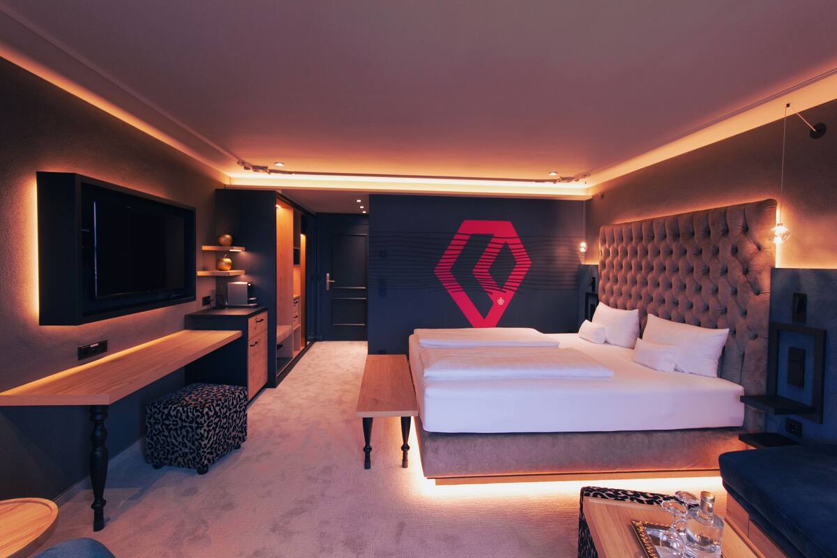 Une chambre d’hôtel moderne équipée d’un grand lit, d’un bureau, d’une télévision et d’un logo fixé au mur.
