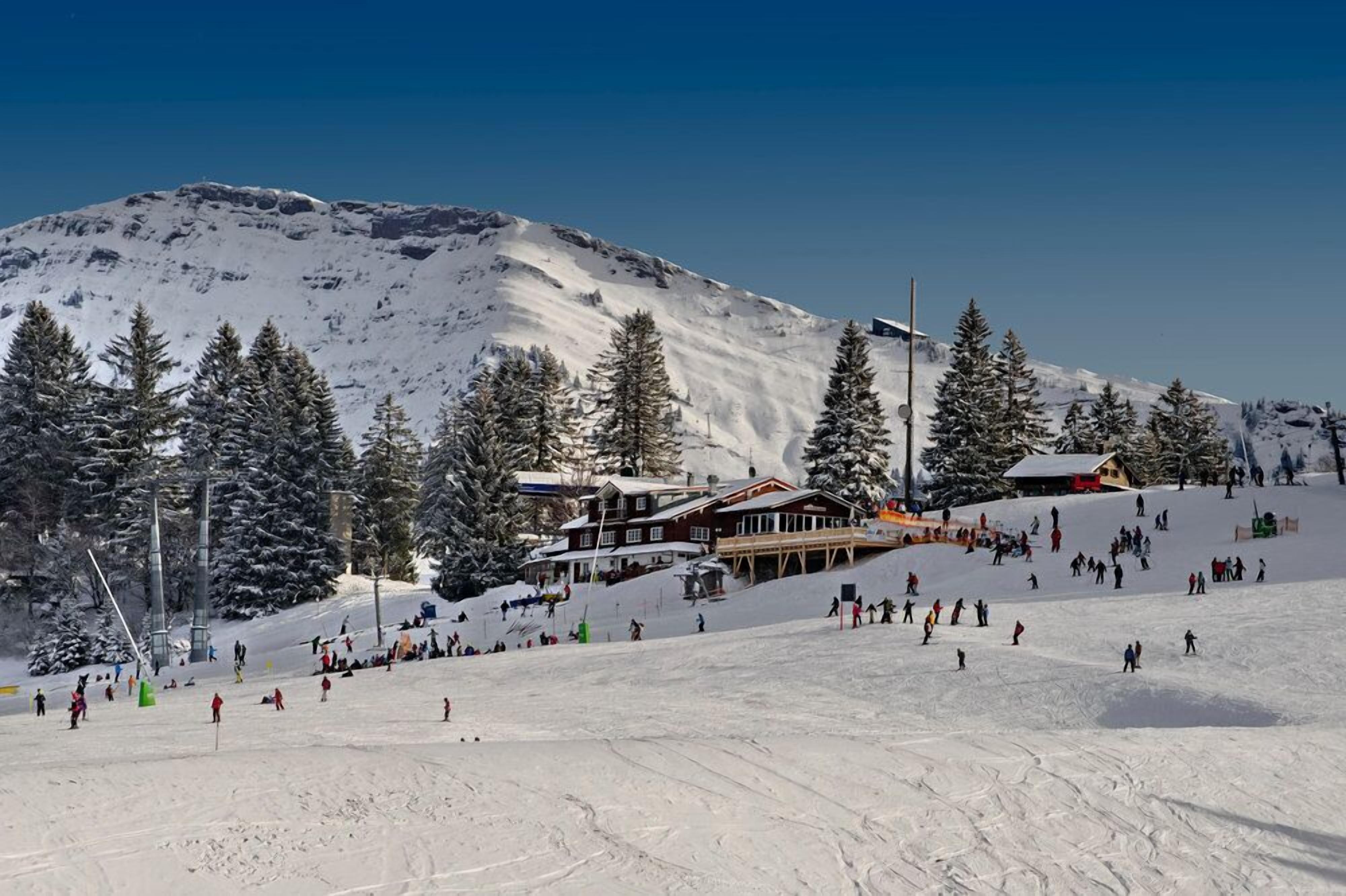 Une station de ski avec un bâtiment situé sur une pente, entouré d’arbres couverts de neige.