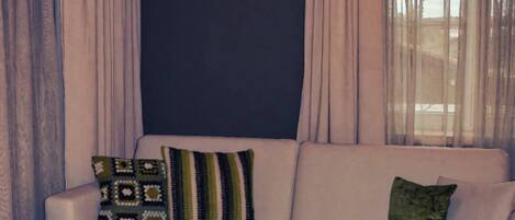 Un salon moderne avec un canapé d’angle, un petit pouf et un luminaire suspendu au plafond.