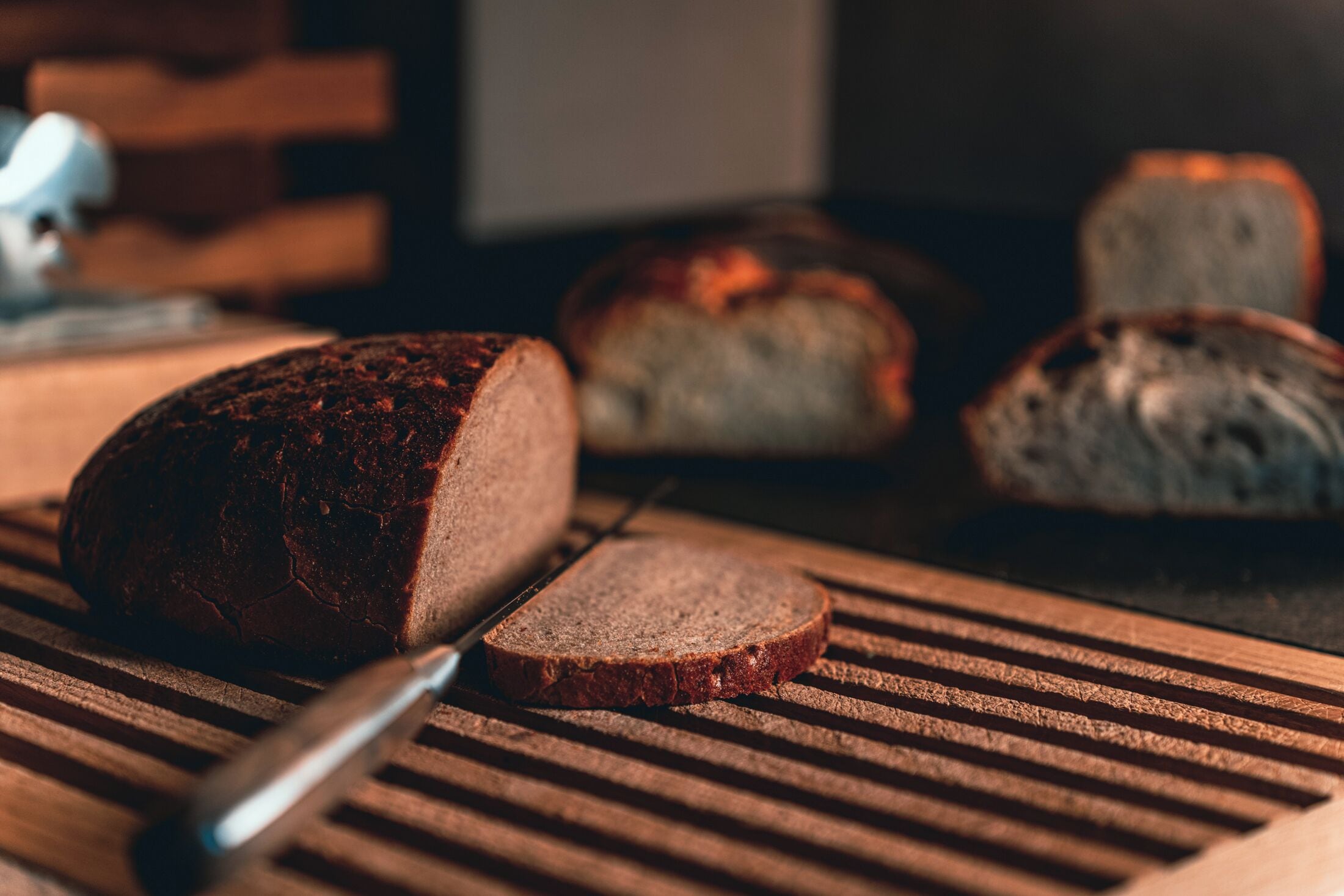 A loaf of dark rye bread on a wooden cutting board with a knife.