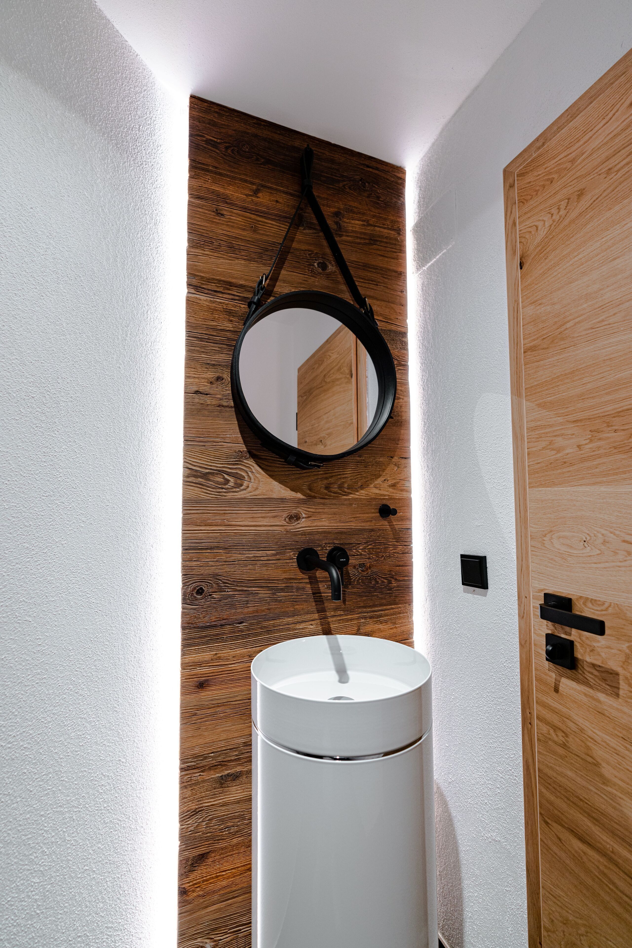 A bathroom with a wooden wall, a round mirror, and a white sink.