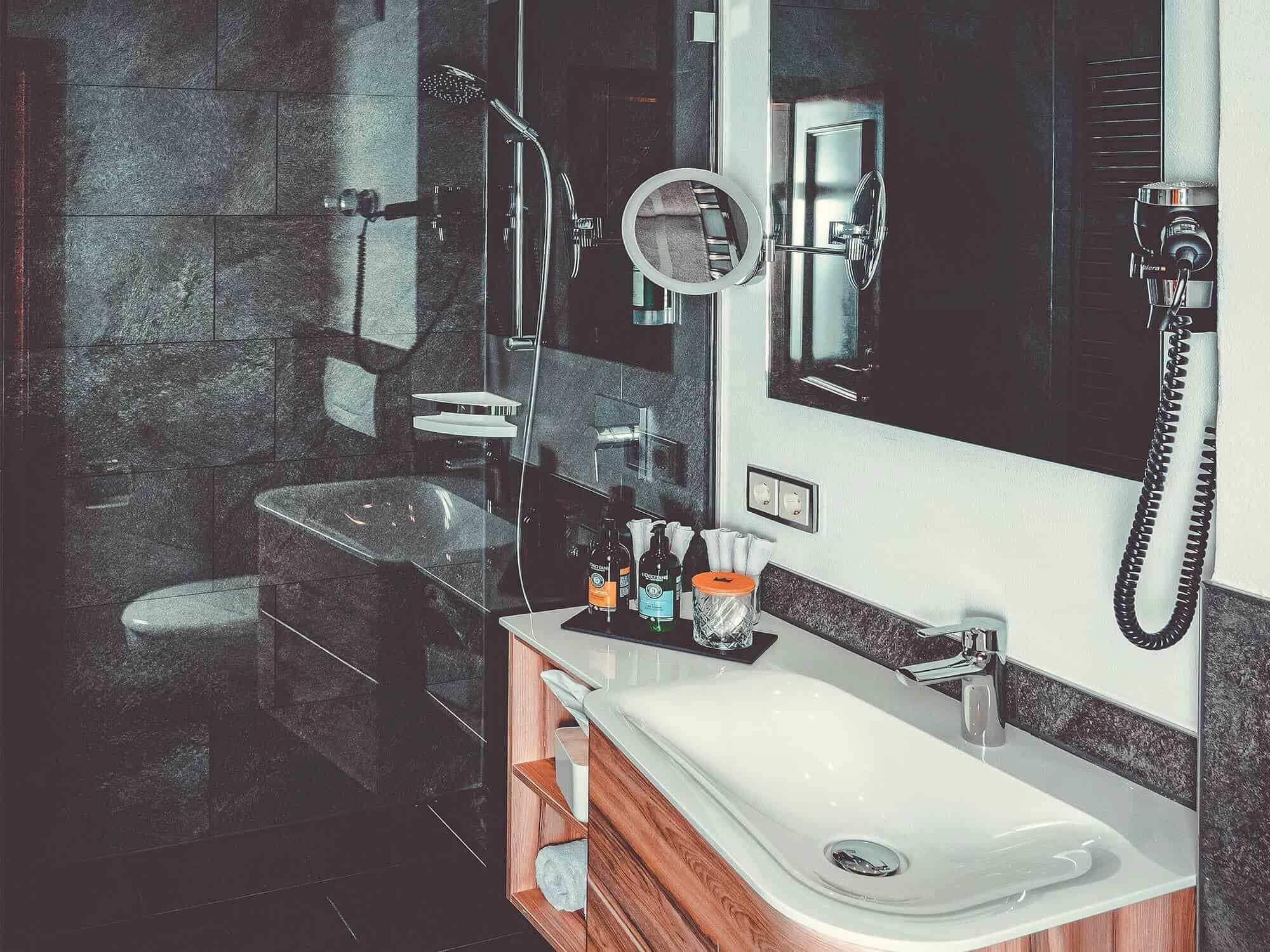 Ein modernes Badezimmer mit einer gläsernen Dusche, einem weißen Waschbecken und einem großen Spiegel.