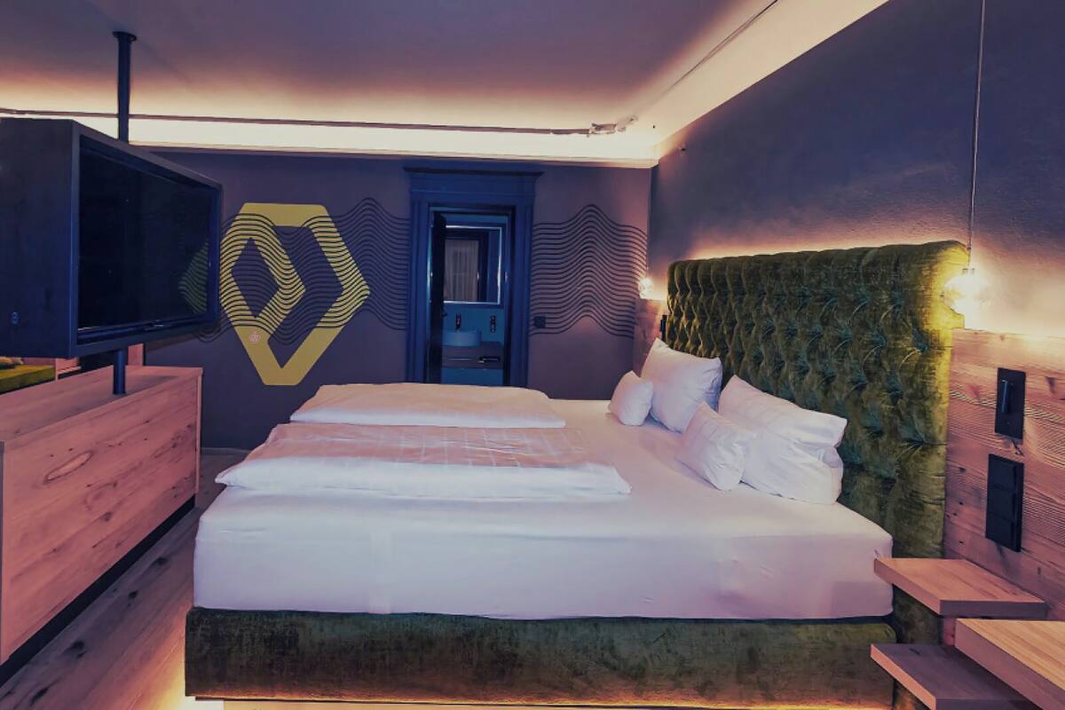 Une chambre d’hôtel moderne avec un grand lit, un téléviseur posé sur une commode en bois et un décor mural original.