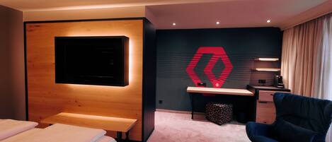 A modern hotel room with a bed, a desk, a chair, and a large wall-mounted TV.