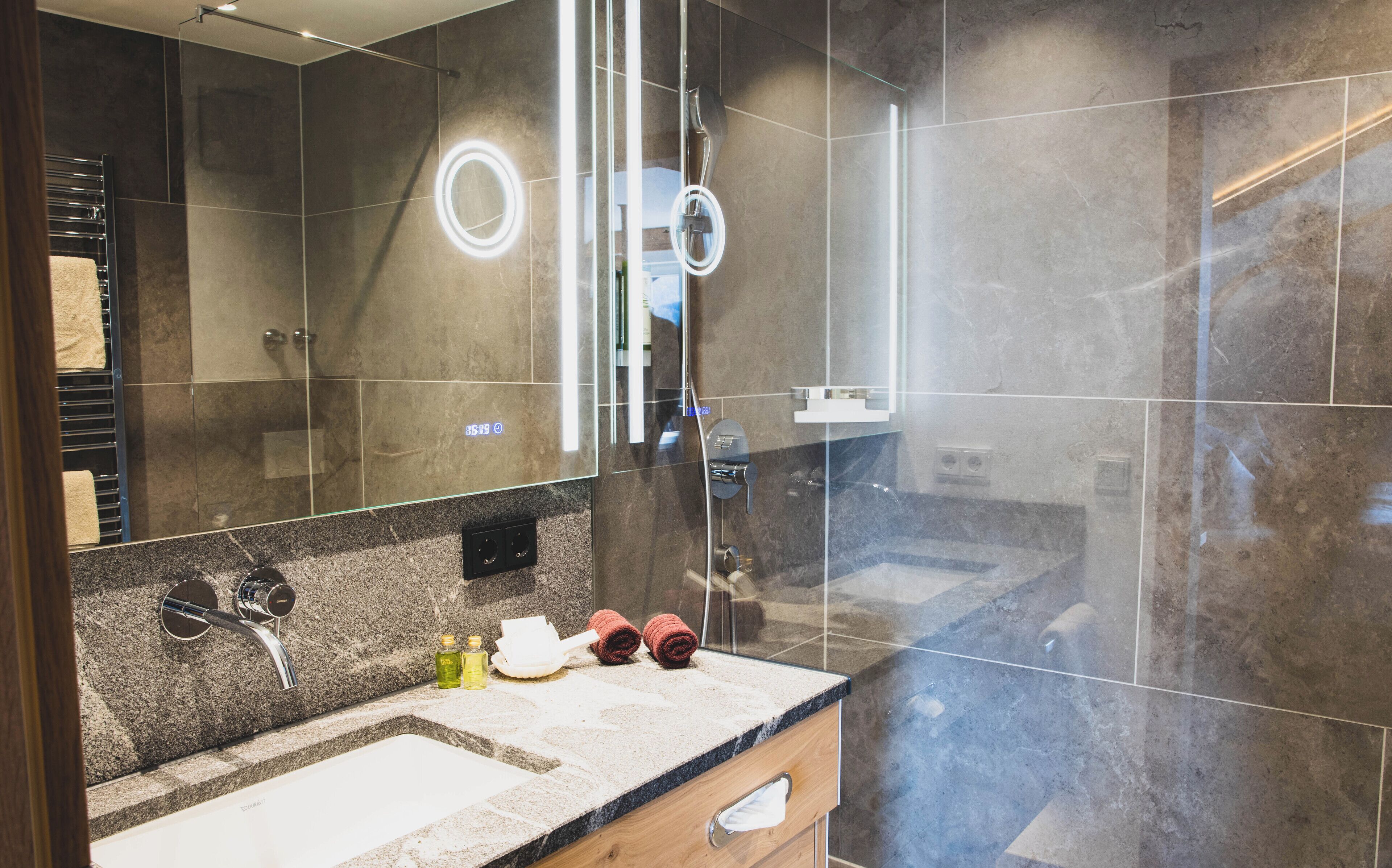A modern bathroom with a glass shower enclosure, a vanity with a sink, and a mirror with a light.