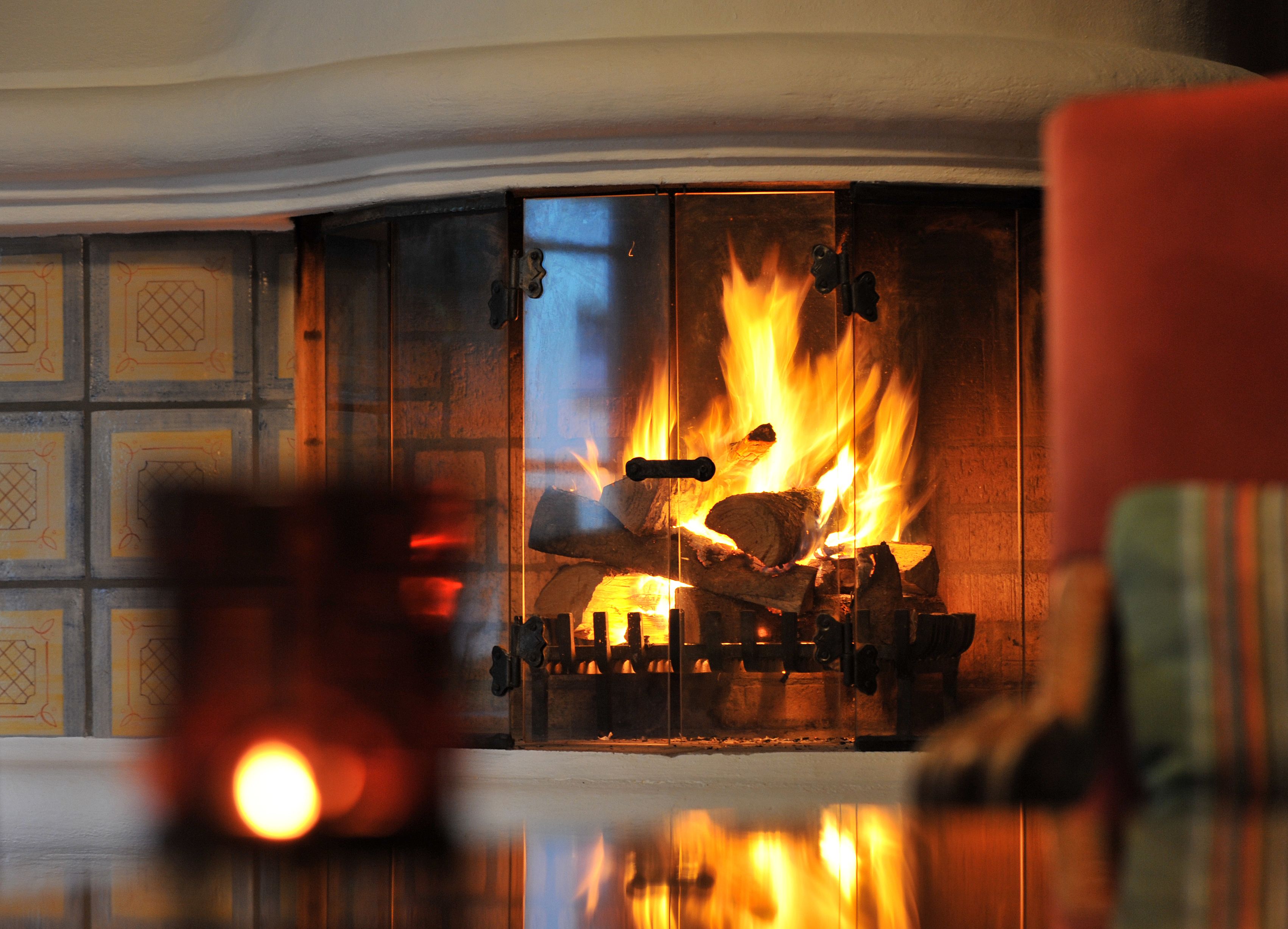 Una chimenea con leña ardiendo y una puerta de cristal que refleja el fuego.
