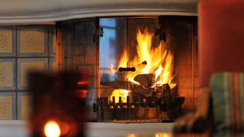 Una chimenea con leña ardiendo y una puerta de cristal que refleja el fuego.