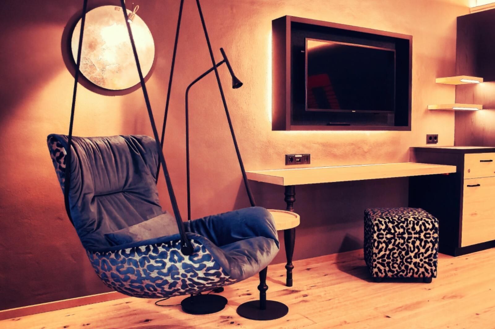 Een moderne kamer met een hangstoel, een bureau, een televisie en een luipaardprint voetenbank.