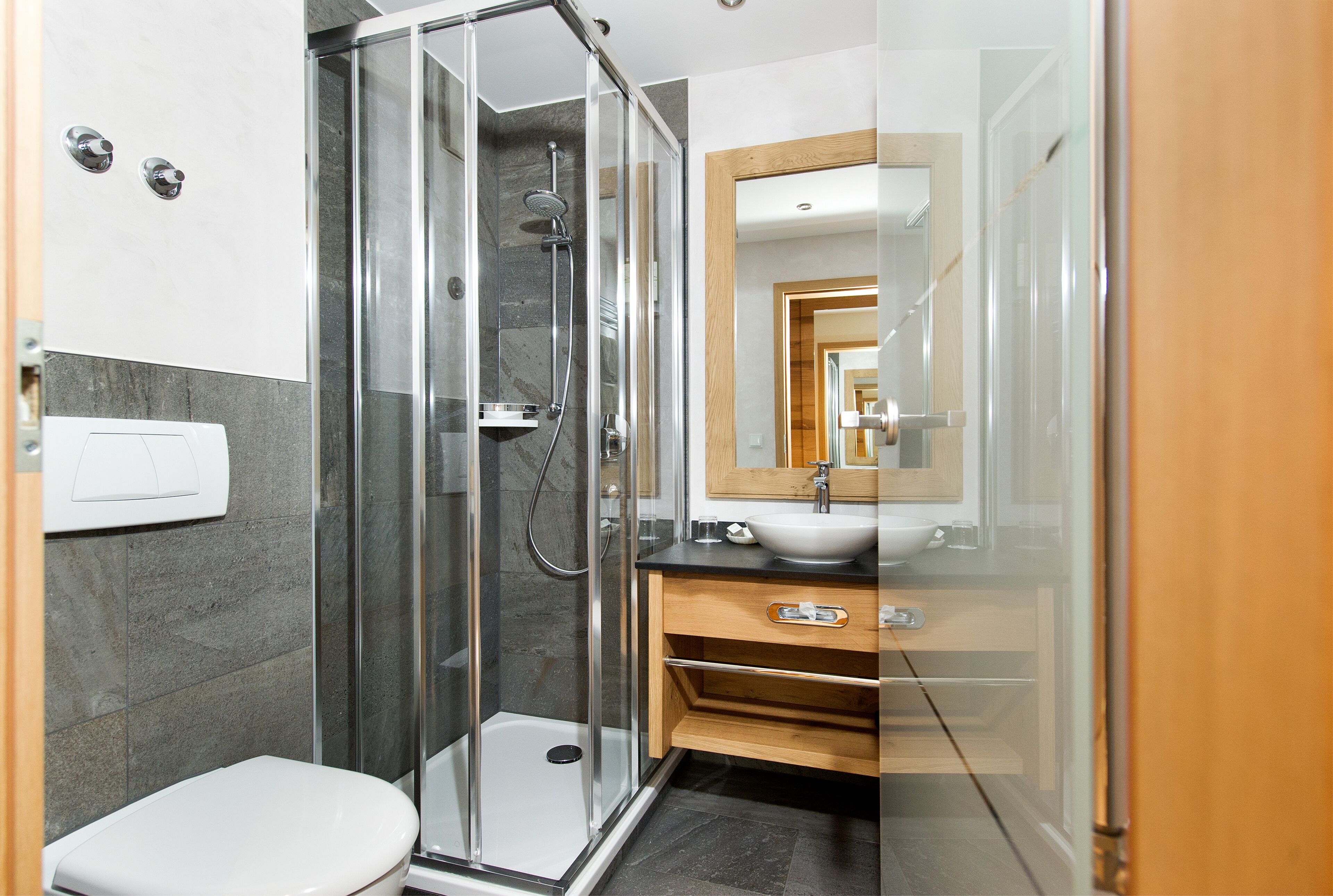 A modern bathroom with a glass-enclosed shower, a white toilet, and a wooden vanity with a sink and mirror.