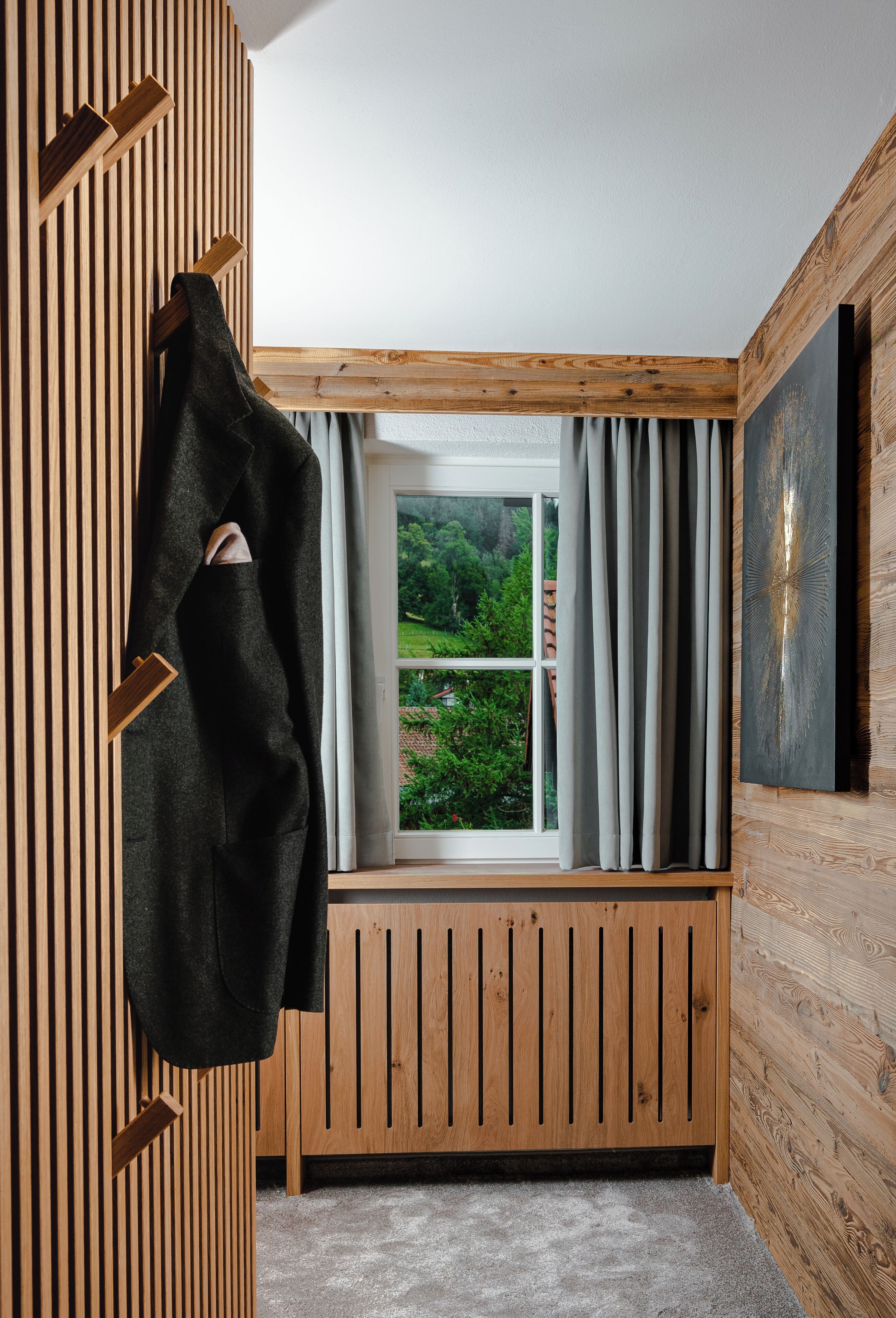 A room with a wooden slatted wall, a window with curtains, and a view of greenery outside.