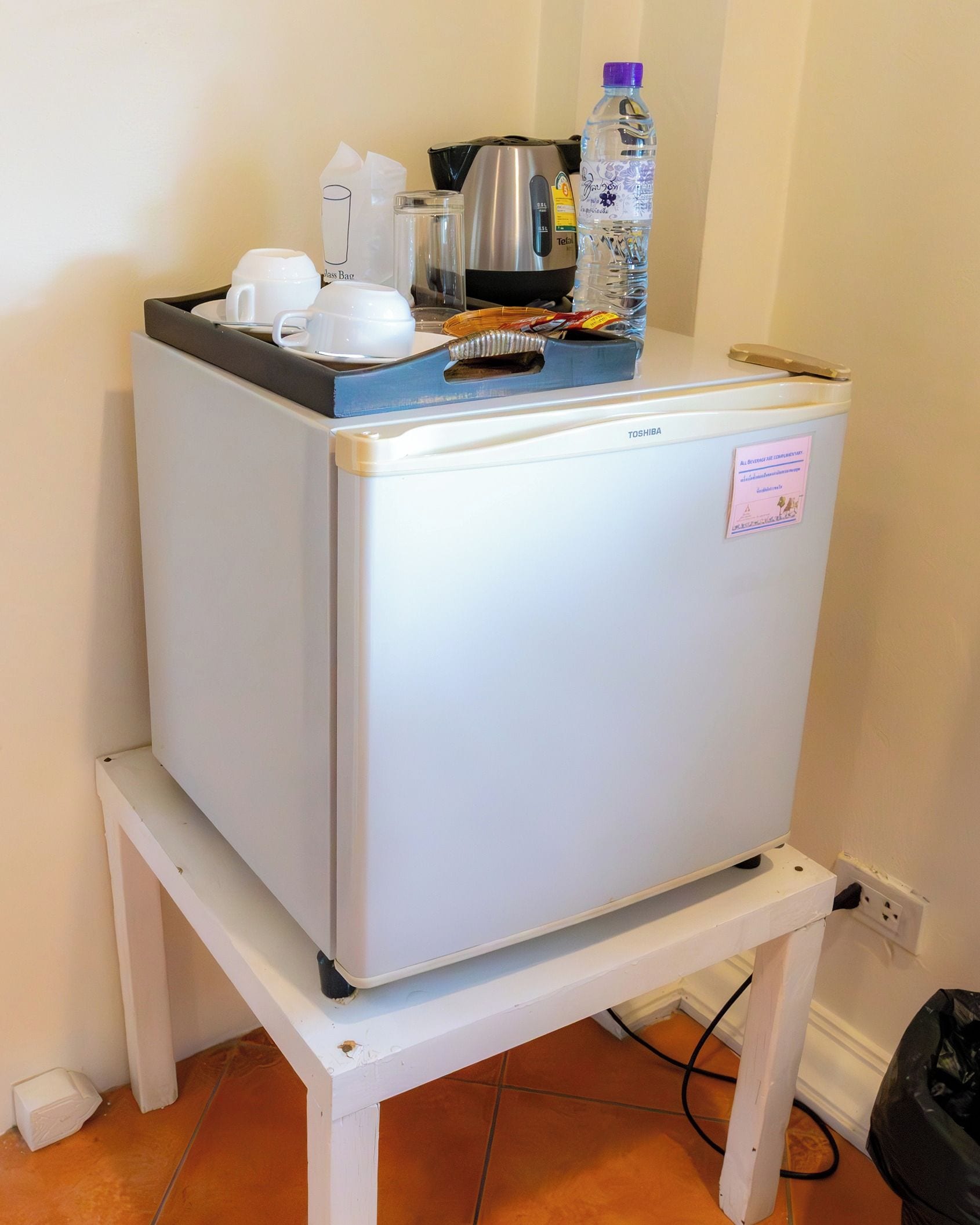 A compact refrigerator on a white table in a room with a tiled floor.