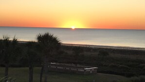 Un coucher de soleil sur l’océan, avec une plage au premier plan.