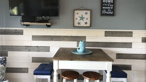 Une pièce avec un téléviseur fixé au mur, une table en bois avec deux tabourets et un mur décoré sur le thème de la marine.
