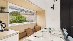 A modern kitchen with a built-in oven, a window overlooking a garden, and a dining area with a white table set for four. - Nice chalet in a residence in St Hilaire (Saint-Hilaire-de-Riez)