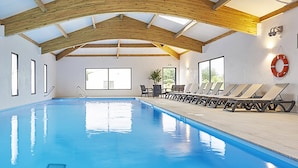 An indoor swimming pool with a wooden ceiling, multiple windows, and sun loungers along the side. - Nice chalet in a residence in St Hilaire (Saint-Hilaire-de-Riez)