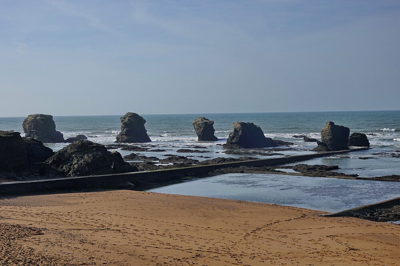 Un paysage côtier avec une plage de sable, des affleurements rocheux et l’océan.
