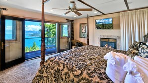 Un dormitorio con una cama grande, ventilador de techo, chimenea y vista al exterior.