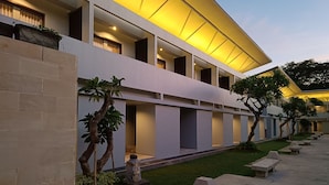 A modern building with a flat roof, multiple balconies, and a well-maintained garden area with benches and trees. - Guna Graha Kuta (Kuta)