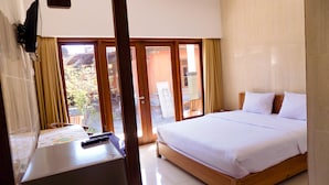 A hotel room with a large bed, a desk with a computer, and a view of the outside. - Guna Graha Kuta (Kuta)