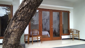 A room with a sliding glass door, two wooden chairs, and a bed. - Guna Graha Kuta (Kuta)