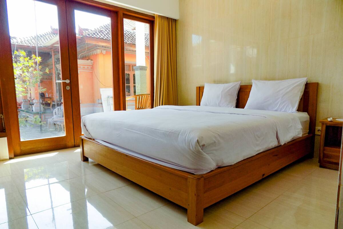 A spacious bedroom with a large bed, a wooden headboard, and a sliding glass door leading to an outdoor area.