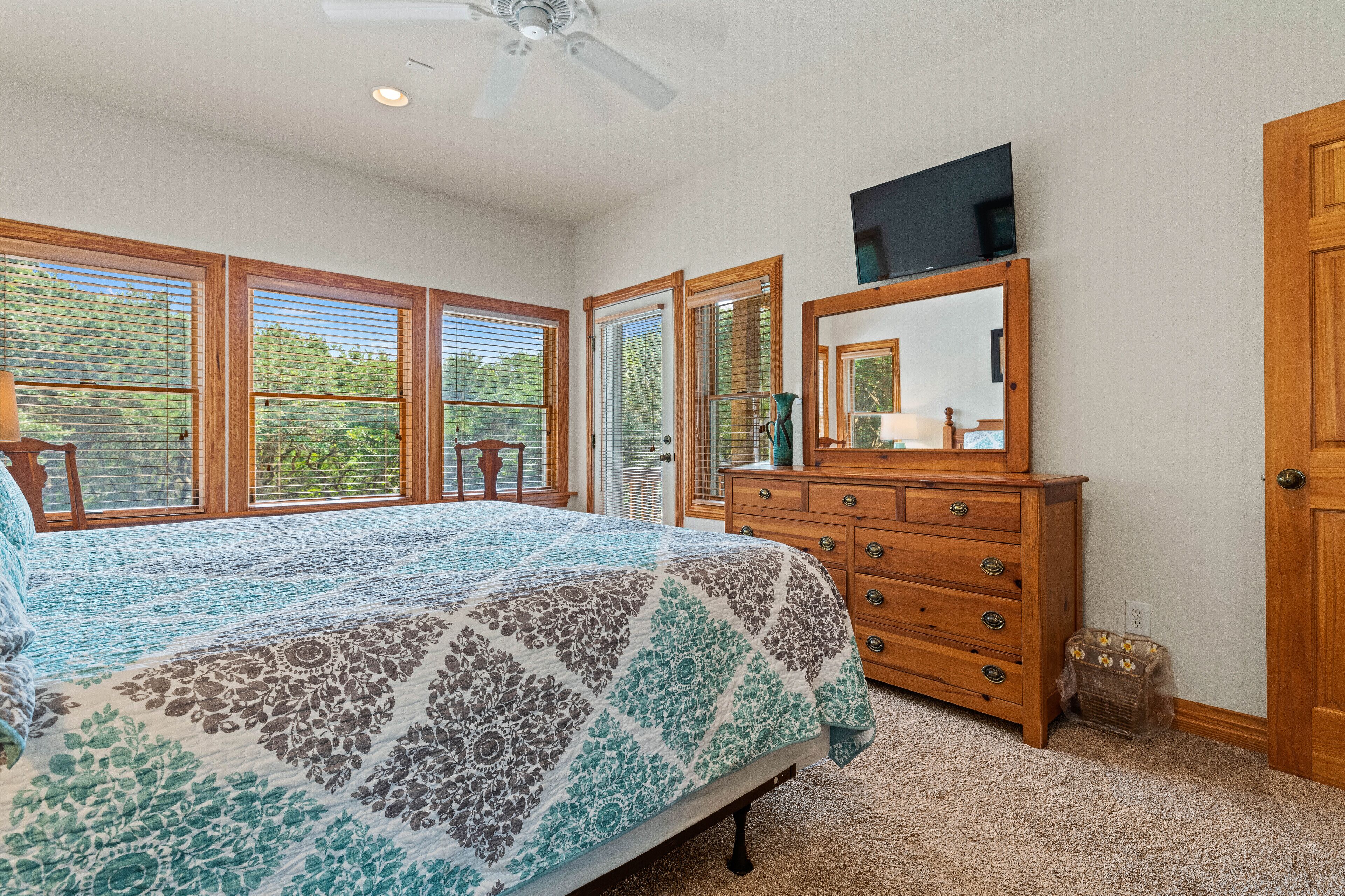A bedroom with a bed, dresser, mirror, and a television on the wall.