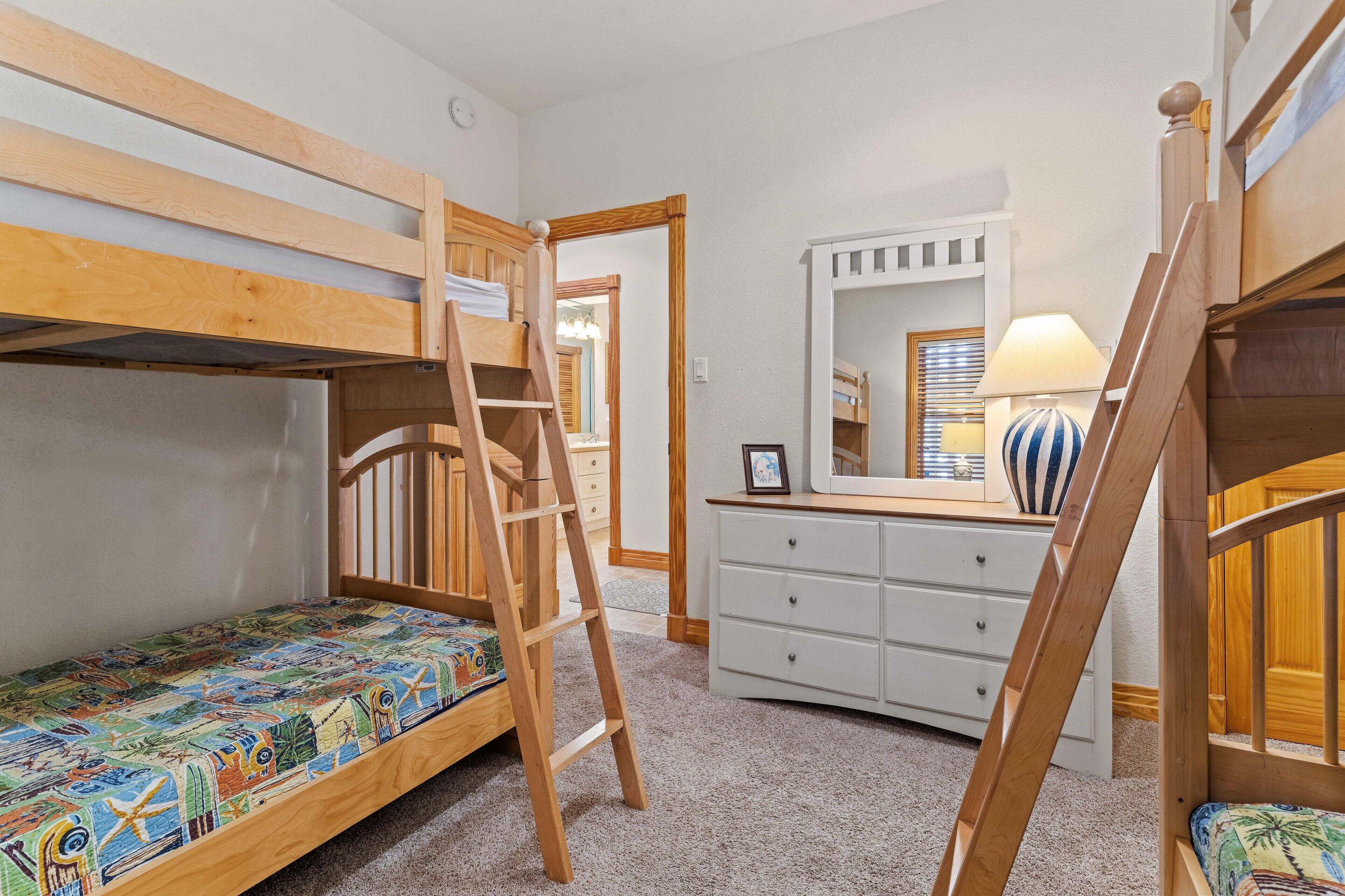 A room with bunk beds, a dresser, a mirror, and a lamp.
