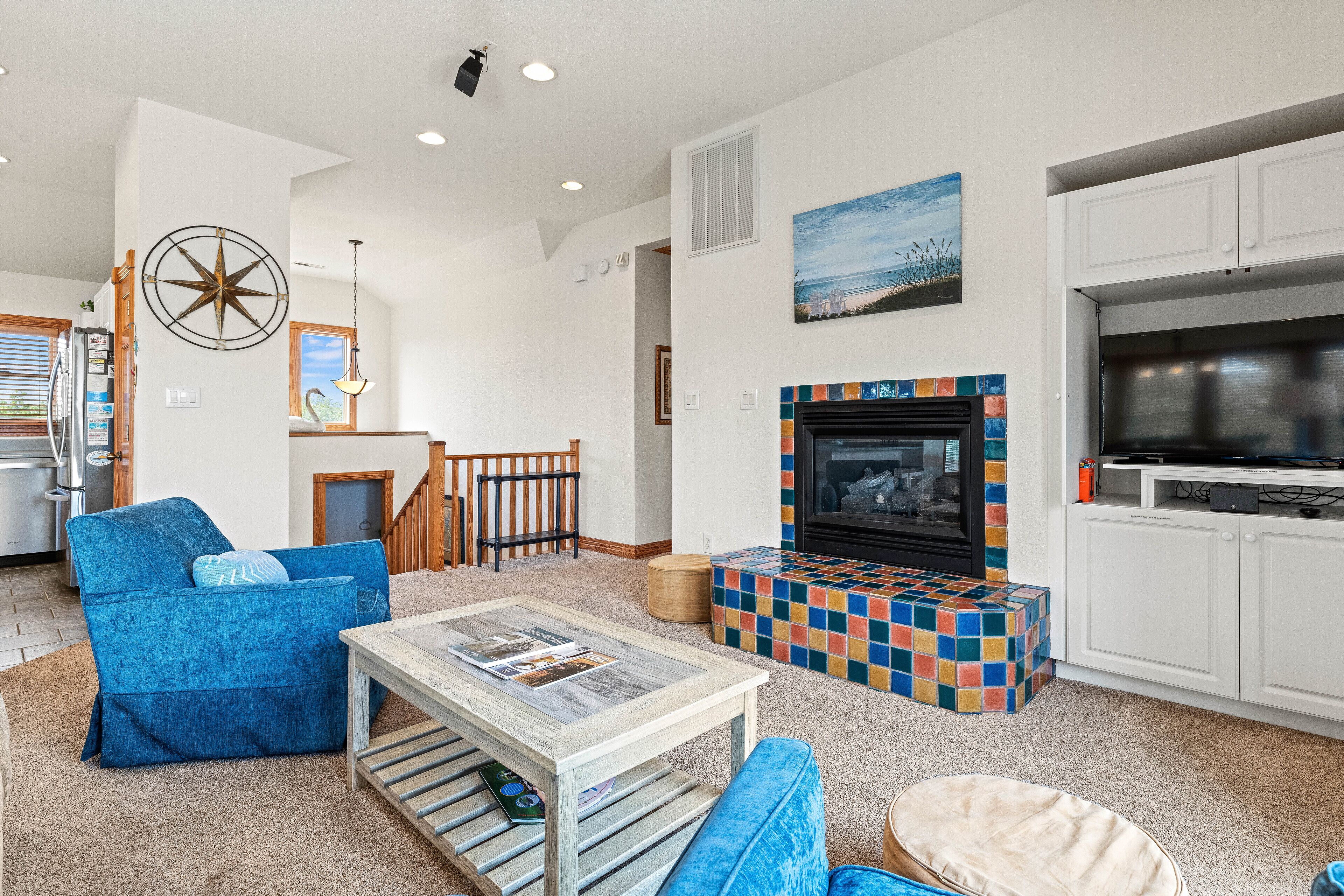 A living room with a fireplace, a blue sofa, a coffee table, and a kitchen area with cabinets and a stove.