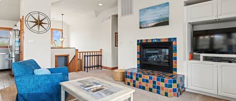 A living room with a fireplace, a blue sofa, a coffee table, and a kitchen area with cabinets and a stove.