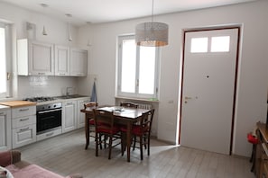 Una cocina moderna con armarios blancos, una mesa de comedor con sillas, una lámpara colgante y una puerta con ventanal.