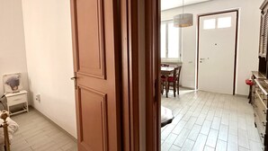 Ein Zimmer mit Holztür, weißer Wand, einem kleinen Nachttisch, einer Lampe und einem Bett.