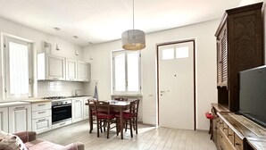 Eine moderne Küche mit weißen Schränken, einem Esstisch mit Stühlen, einer Hängeleuchte und einem Fernseher auf einem Holzschrank.
