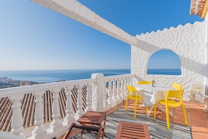 A terrace with a white balustrade, a table with yellow chairs, and a view of the sea.
