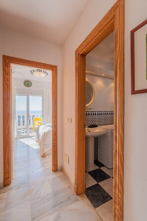 A hotel room with a balcony, a bed, a bathroom with a sink and mirror, and a hallway with a checkered floor.