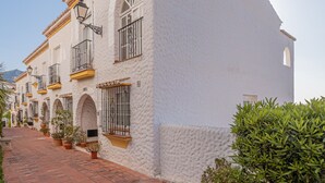 A row of white buildings with terracotta tiled roofs and arched windows, lined with potted plants.