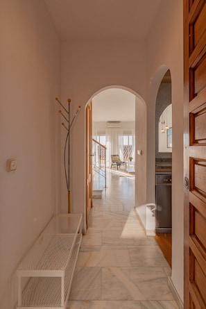 A hallway with a bench, an archway leading to a living area, and a kitchen area visible through the archway.