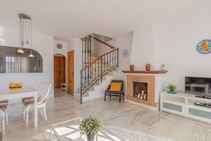 A spacious living area with a fireplace, a dining table with chairs, a staircase, and a television.