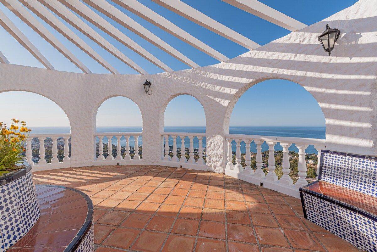 A terrace with a tiled floor, white arches, and a view of the sea.