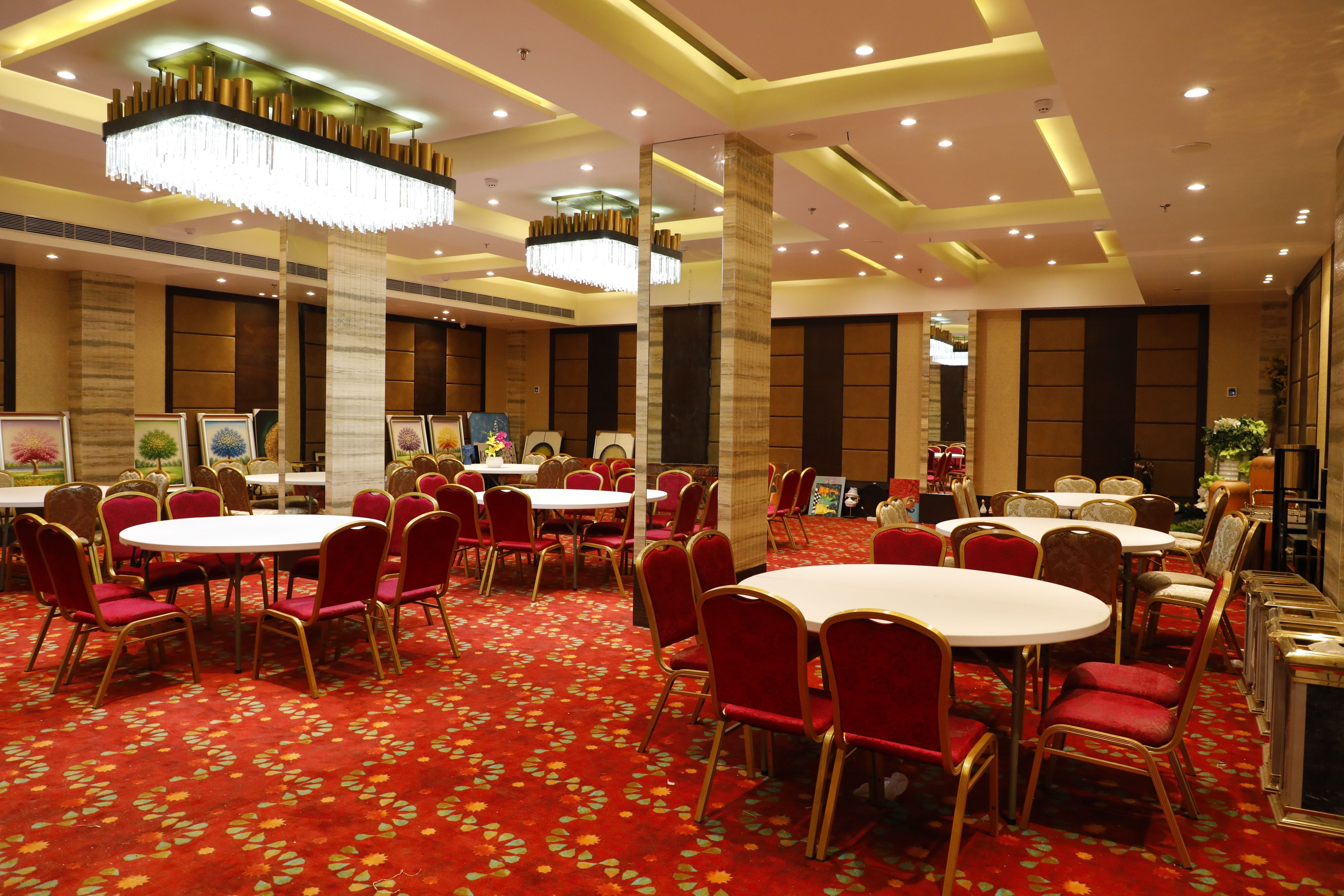 Un salón de conferencias de hotel con mesas redondas y sillas rojas, grandes candelabros y suelo cubierto de alfombra roja.