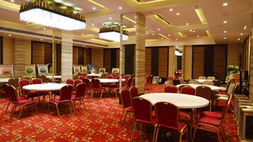 Un salón de conferencias de hotel con mesas redondas y sillas rojas, grandes candelabros y suelo cubierto de alfombra roja.