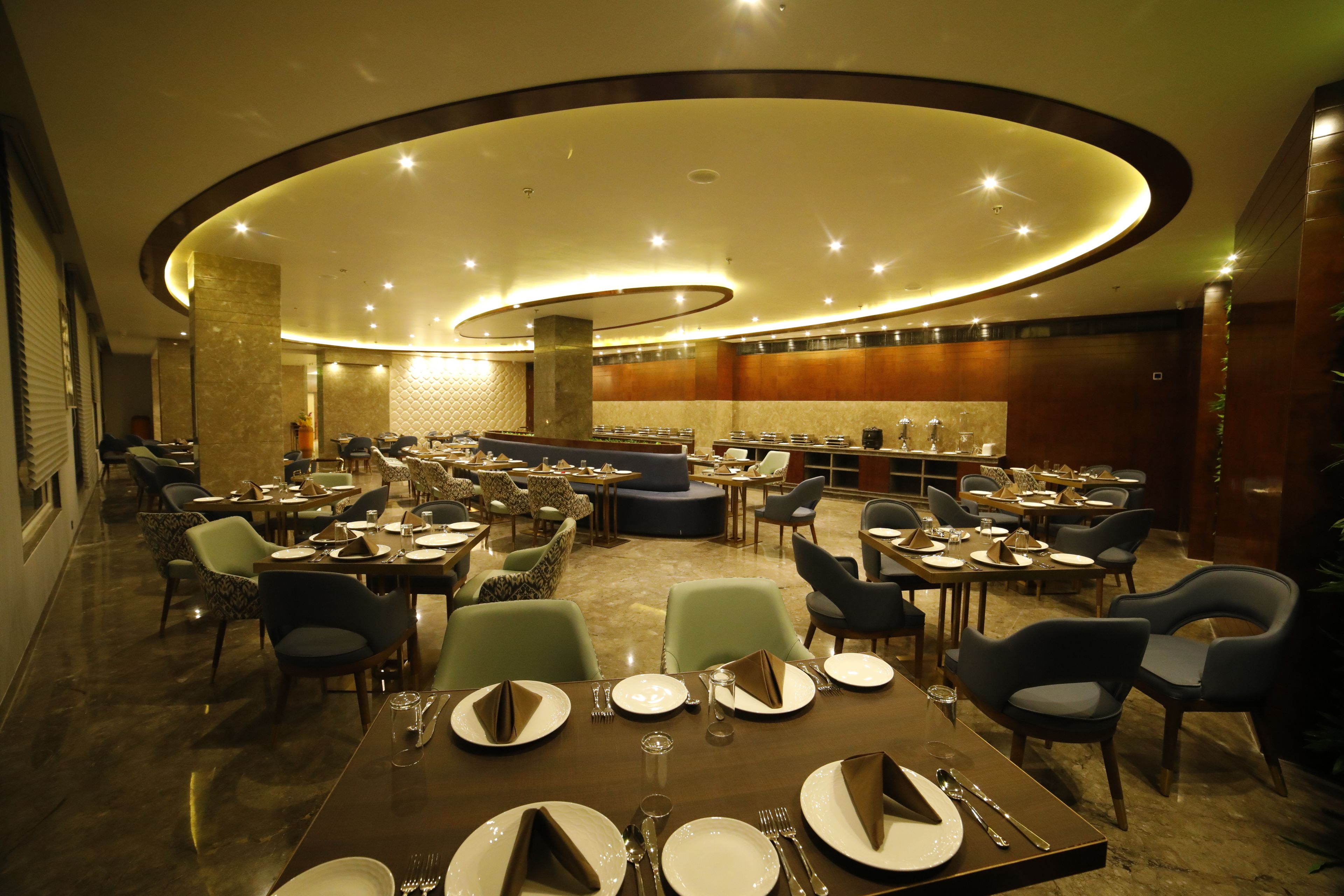 Un ristorante spazioso con diversi tavoli e sedie, un'area salotto centrale e un moderno design del soffitto.