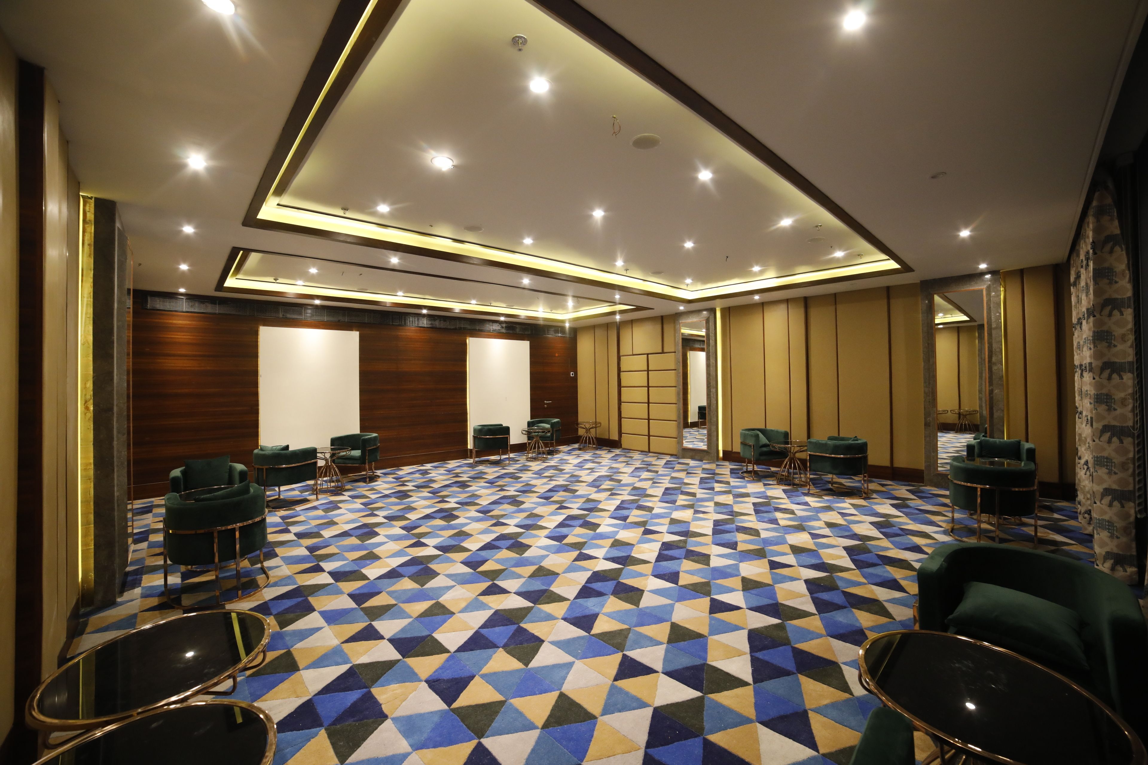 A conference room with a geometric patterned carpet, green upholstered chairs, and a modern ceiling design.
