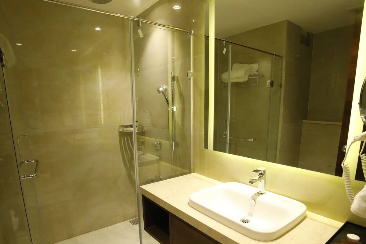 Un baño moderno con ducha envuelta en vidrio, un lavamanos blanco y un espejo grande.