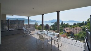 Un balcón con una mesa para dos, con vistas a un paisaje montañoso y un lago.